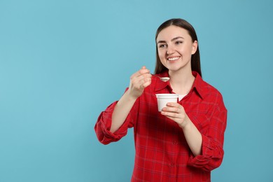 Woman with tasty yogurt on light blue background, space for text