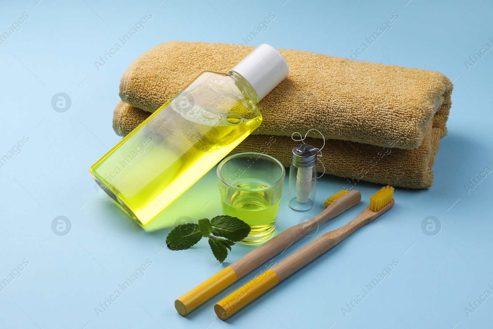 Photo of Fresh mouthwash, towel, toothbrushes and dental floss on light blue background, closeup