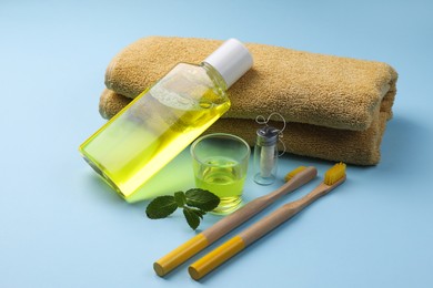 Fresh mouthwash, towel, toothbrushes and dental floss on light blue background, closeup