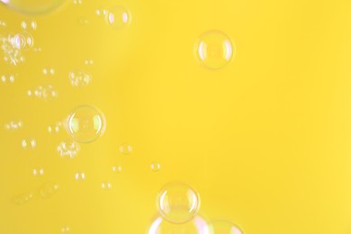 Beautiful transparent soap bubbles on yellow background, space for text