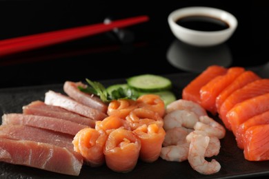Photo of Delicious sashimi set of salmon, tuna and shrimps served with cucumbers, parsley and soy sauce on black serving board, closeup