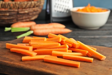 Photo of Wooden board with carrot sticks on table