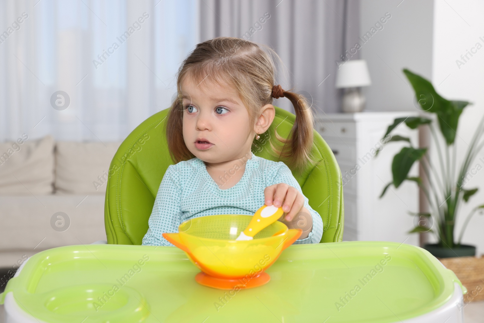 Photo of Cute little child with bowl of tasty yogurt in high chair indoors