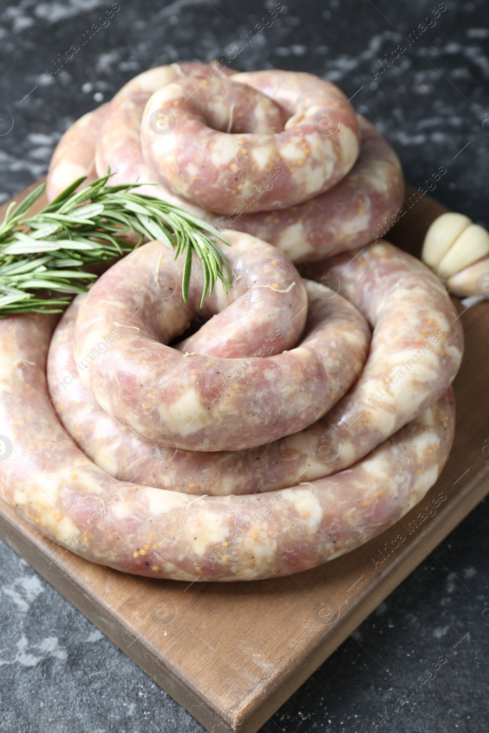 Photo of Raw homemade sausage, rosemary and garlic on grey textured table, closeup