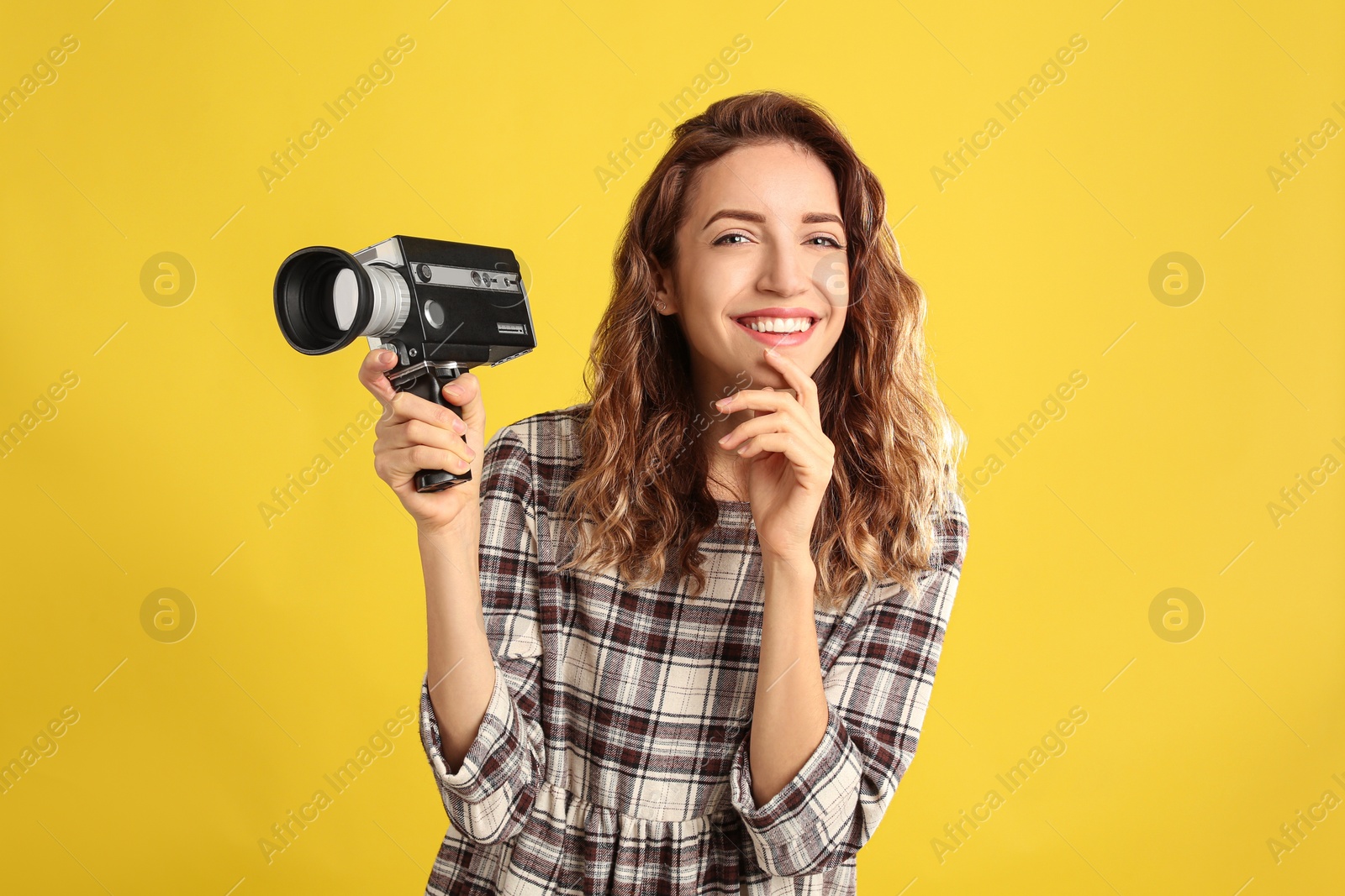 Photo of Beautiful young woman with vintage video camera on yellow background