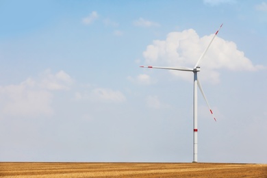 Modern wind turbine in field against blue sky. Energy efficiency