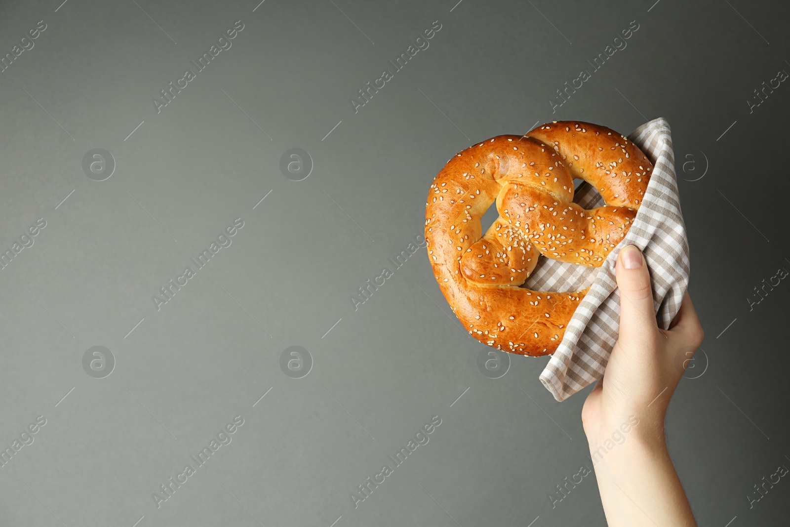 Photo of Woman with tasty freshly baked pretzel on grey background, closeup. Space for text
