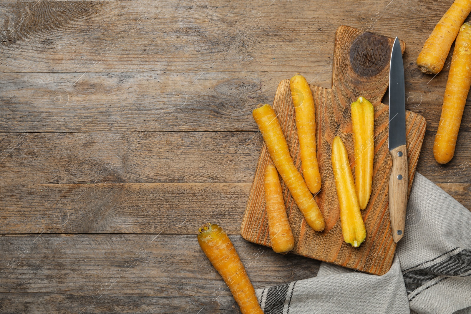 Photo of Raw yellow carrots, cutting board and knife on wooden table, flat lay. Space for text