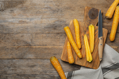 Photo of Raw yellow carrots, cutting board and knife on wooden table, flat lay. Space for text