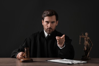 Judge with gavel pointing at wooden table against black background