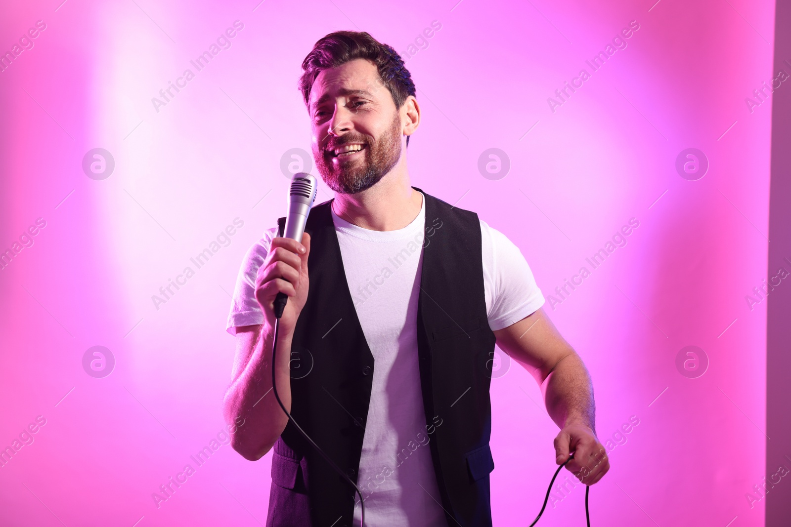 Photo of Handsome man with microphone singing on pink background