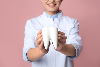 Photo of Female dentist holding tooth model on color background, closeup