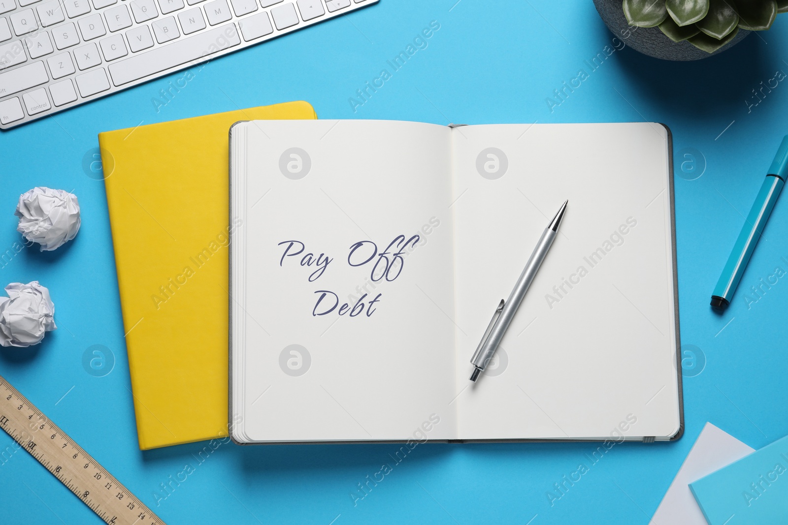 Image of Notebook with phrase Pay Off Debt and pen on light blue background, flat lay