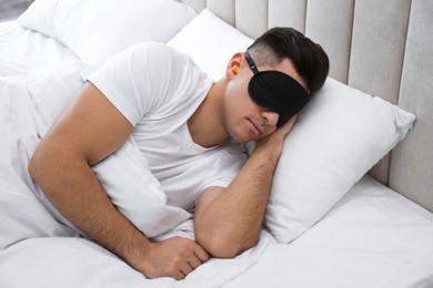 Photo of Man with foam ear plugs and mask sleeping in bed