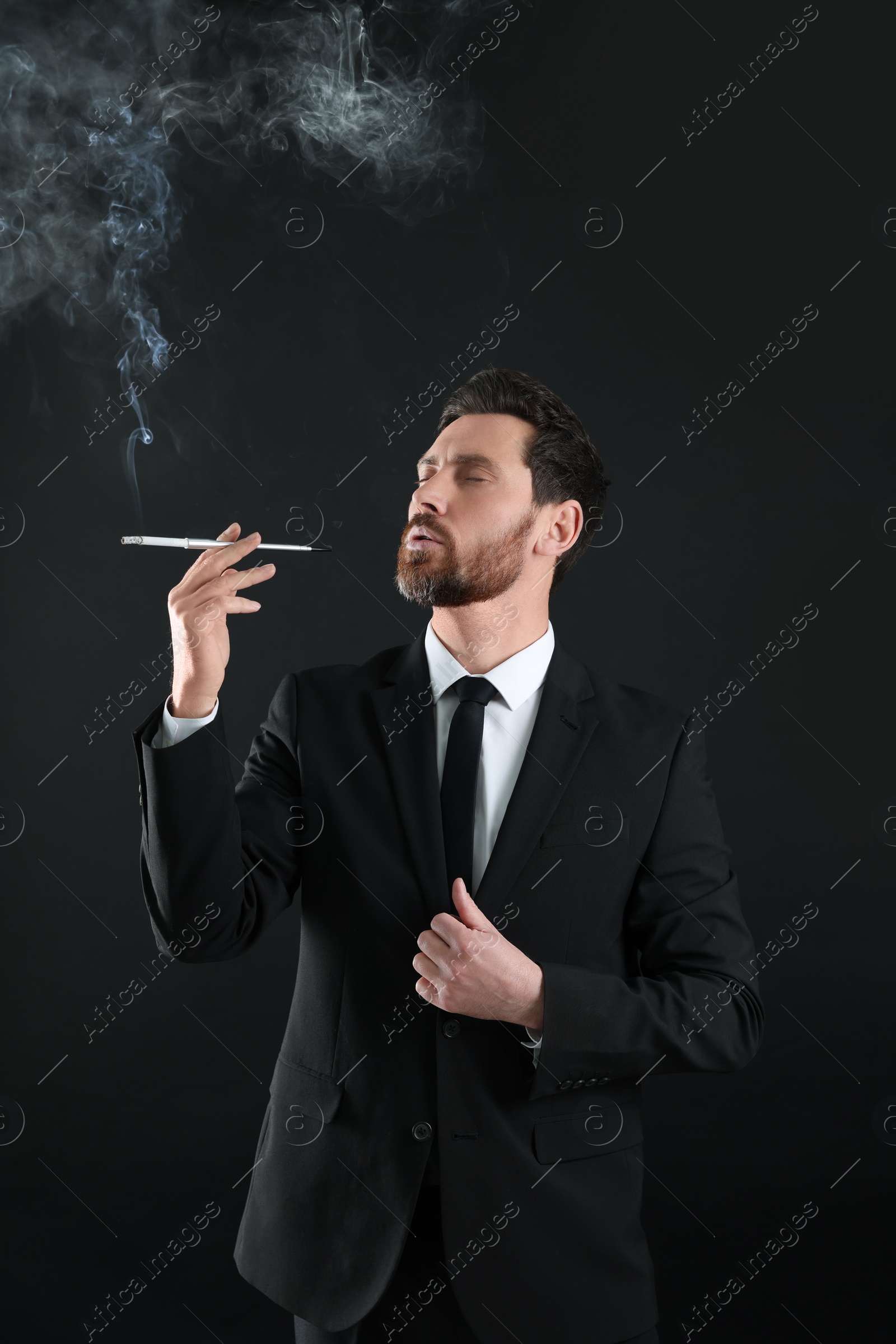 Photo of Man using long cigarette holder for smoking on black background