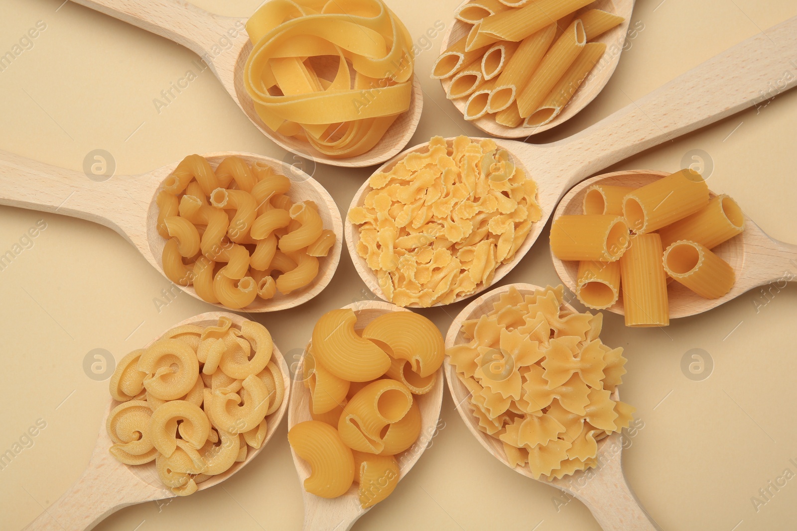 Photo of Different types of pasta in spoons on beige background, flat lay