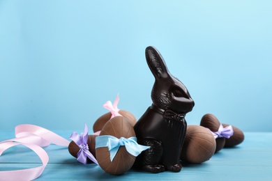 Photo of Dark chocolate Easter bunny and eggs on light blue wooden table. Space for text