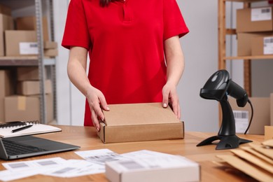 Photo of Post office worker packing parcel at wooden table indoors, closeup