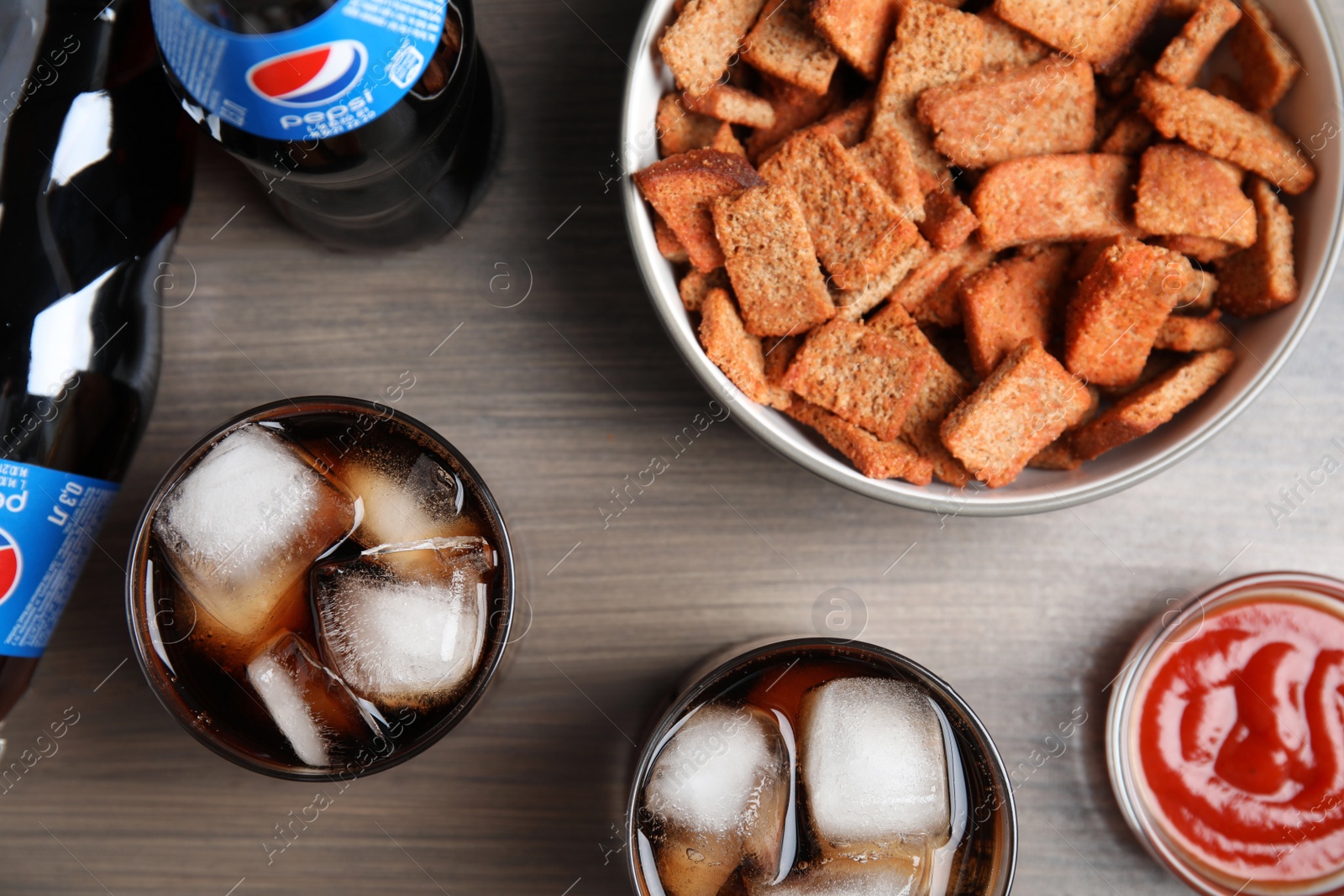 Photo of MYKOLAIV, UKRAINE - FEBRUARY 15, 2021: Glasses and bottles of Pepsi with snack on wooden table, flat lay