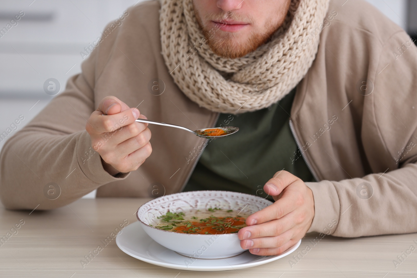 Photo of Sick young man eating soup to cure flu at table indoors