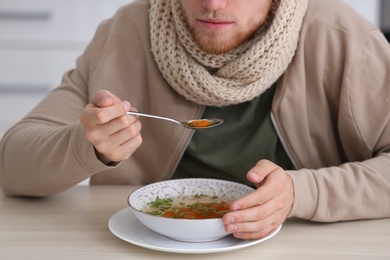 Photo of Sick young man eating soup to cure flu at table indoors