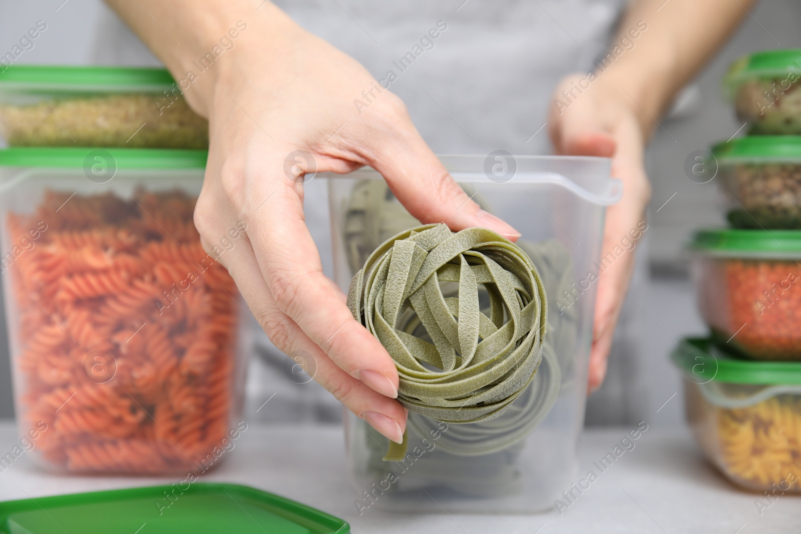 Photo of Woman with raw pasta and plastic filled containers of other food products at light table indoors, selective focus