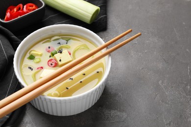 Photo of Bowl of delicious miso soup with tofu and chopsticks served on grey table. Space for text