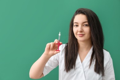 Cosmetologist with syringe on green background, space for text
