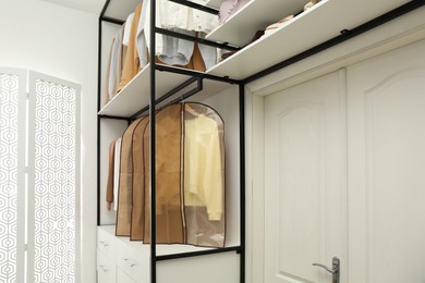 Photo of Garment bags with clothes on rack in dressing room. Space for text