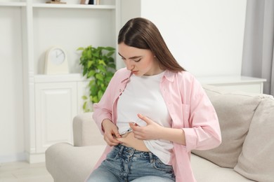 Photo of Diabetes. Woman making insulin injection into her belly on sofa at home