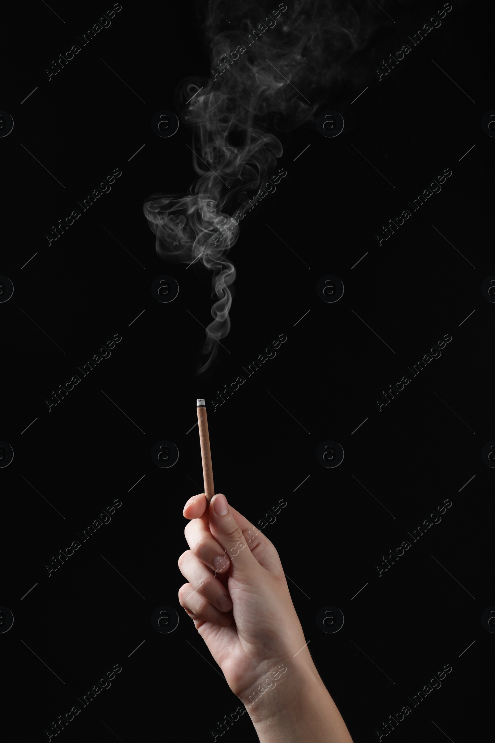 Photo of Woman holding smoldering incense stick on black background, closeup