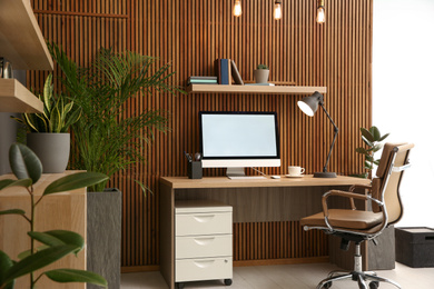 Photo of Comfortable workplace with computer near wooden wall in stylish room interior. Home office design