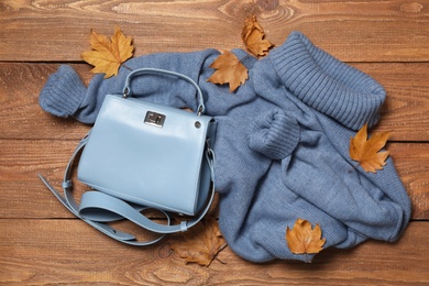 Photo of Warm sweater, bag and dry leaves on wooden background, flat lay. Autumn season