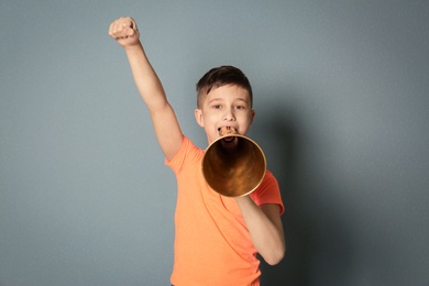 Cute little boy with megaphone on grey background