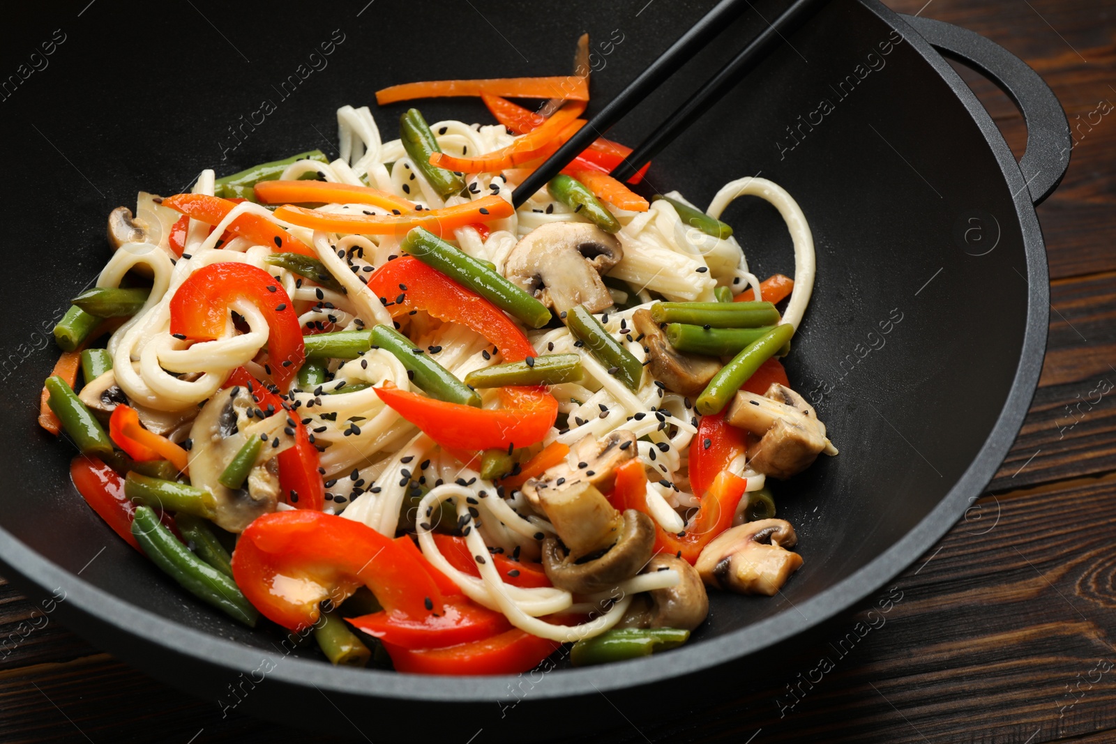 Photo of Stir fried noodles with mushrooms and vegetables in wok on wooden table, closeup