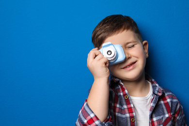 Photo of Little photographer taking picture with toy camera on blue background. Space for text