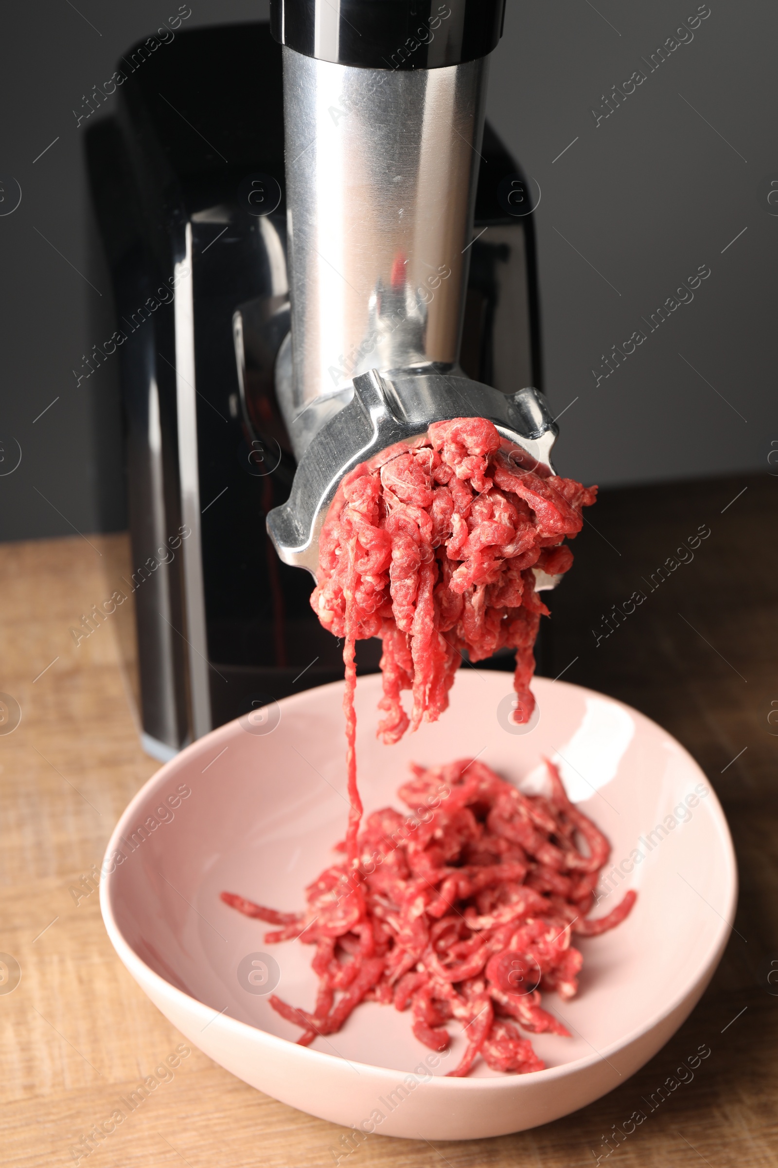 Photo of Electric meat grinder with beef mince on wooden table