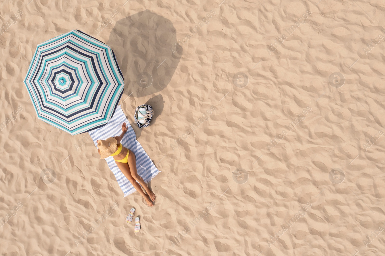 Image of Woman resting under striped beach umbrella at sandy coast, aerial view. Space for text