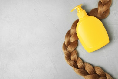 Photo of Blank bottle of cosmetic product and braided hair on light background, flat lay. Space for design