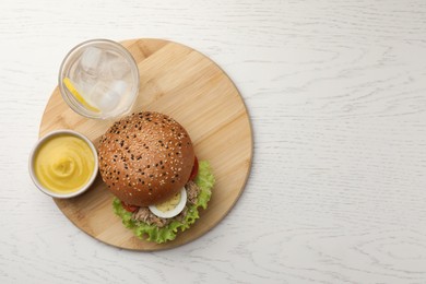 Photo of Delicious sandwich with tuna, boiled egg, vegetables served with mustard sauce and water with lemon on white wooden table, top view. Space for text