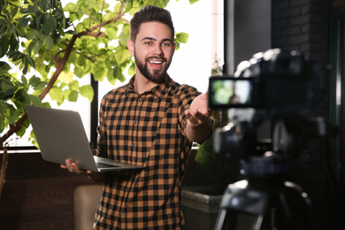 Photo of Young blogger with laptop recording video on camera indoors