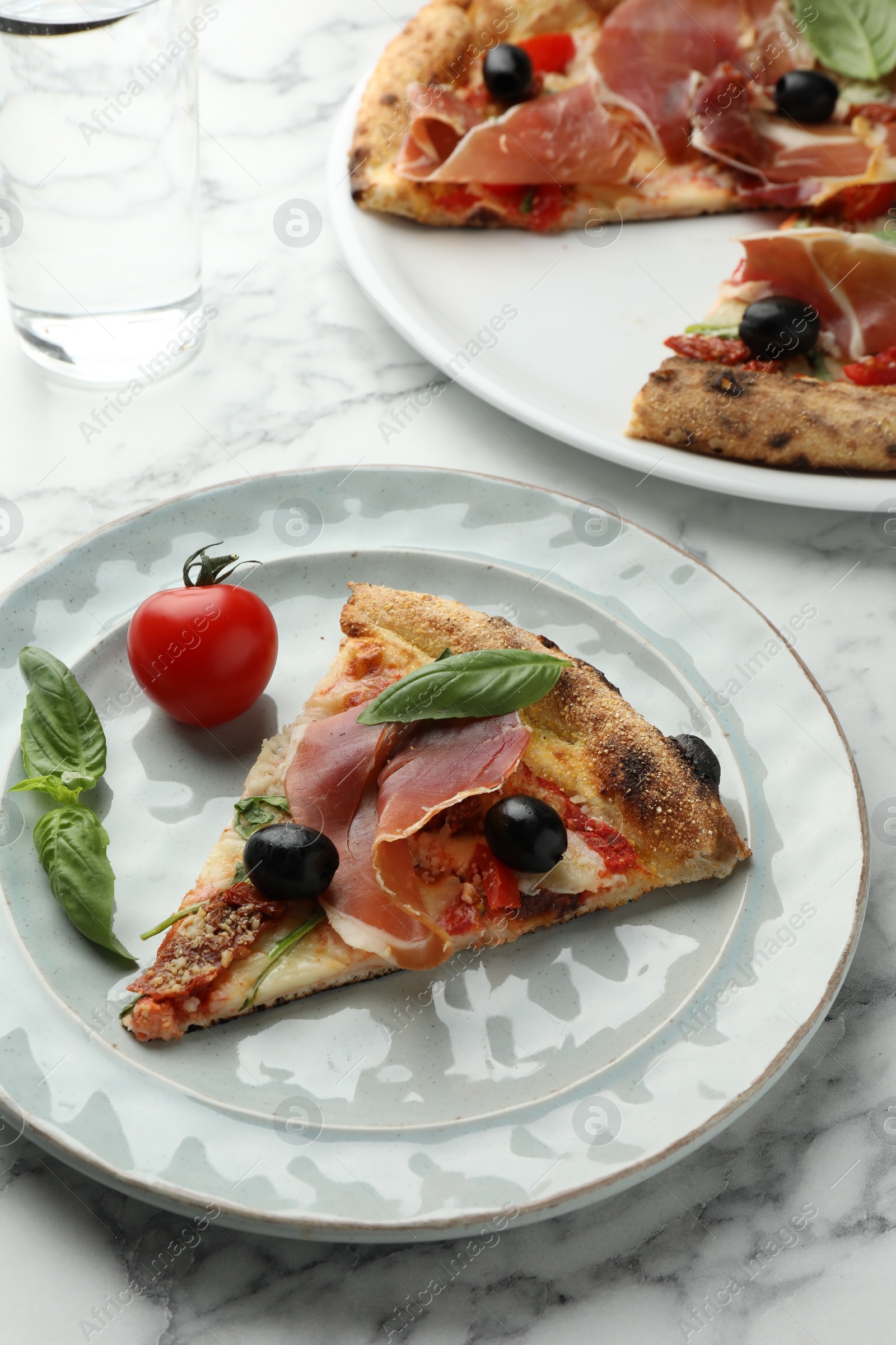 Photo of Tasty pizza with cured ham, olives, tomato and basil on white table