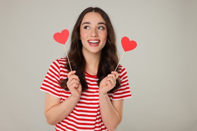 Beautiful young woman with paper hearts on grey background