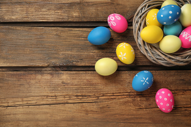 Photo of Colorful Easter eggs in decorative nest on wooden background, flat lay. Space for text