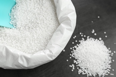 Photo of Bag with granular mineral fertilizer and scoop on grey background, closeup