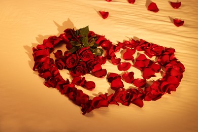 Photo of Honeymoon. Heart made with roses and beautiful petals on bed