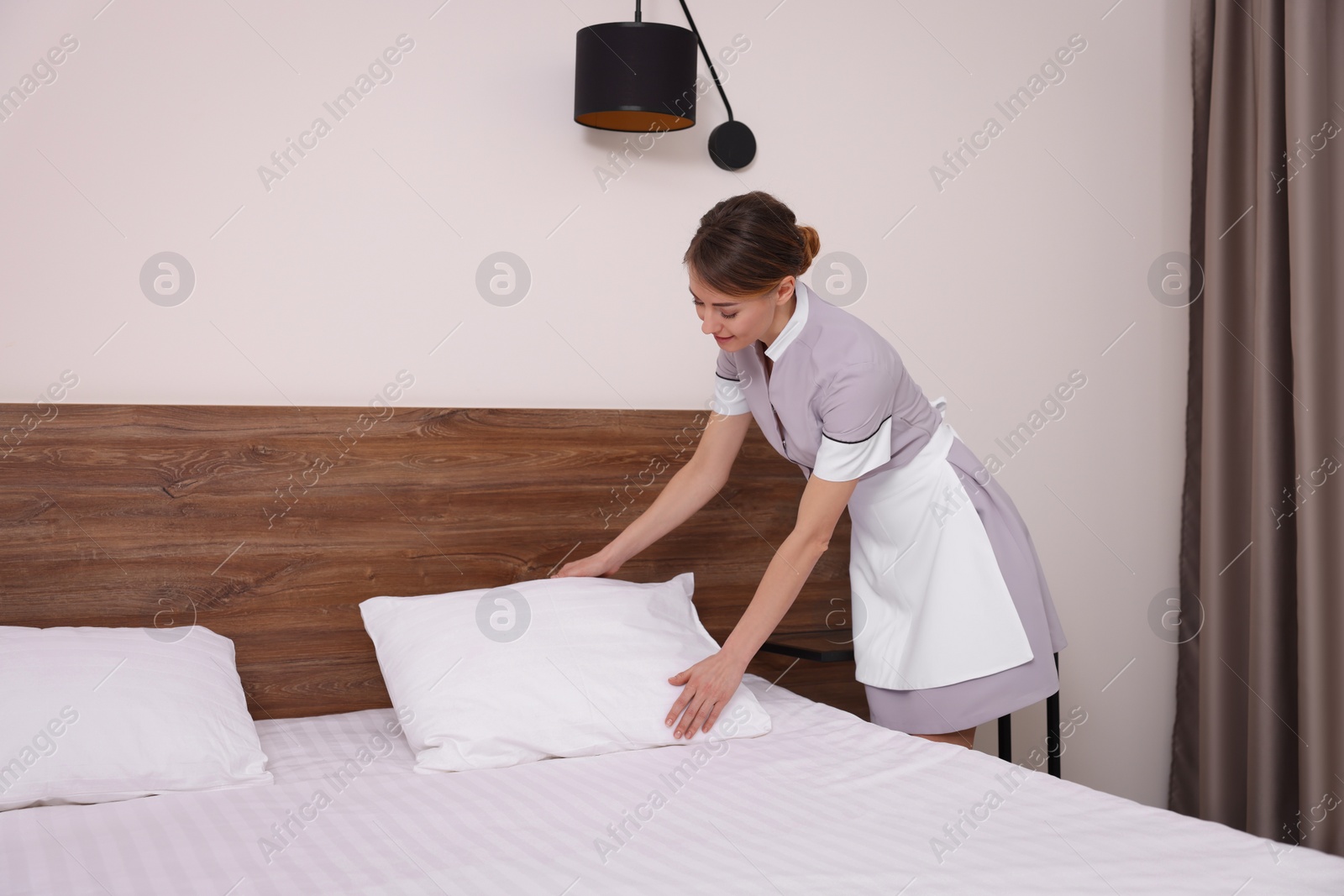 Photo of Beautiful chambermaid making bed in hotel room