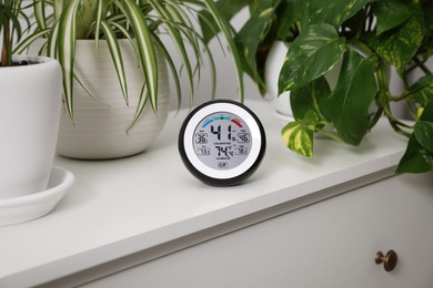 Photo of Digital hygrometer with thermometer and plants on chest of drawers
