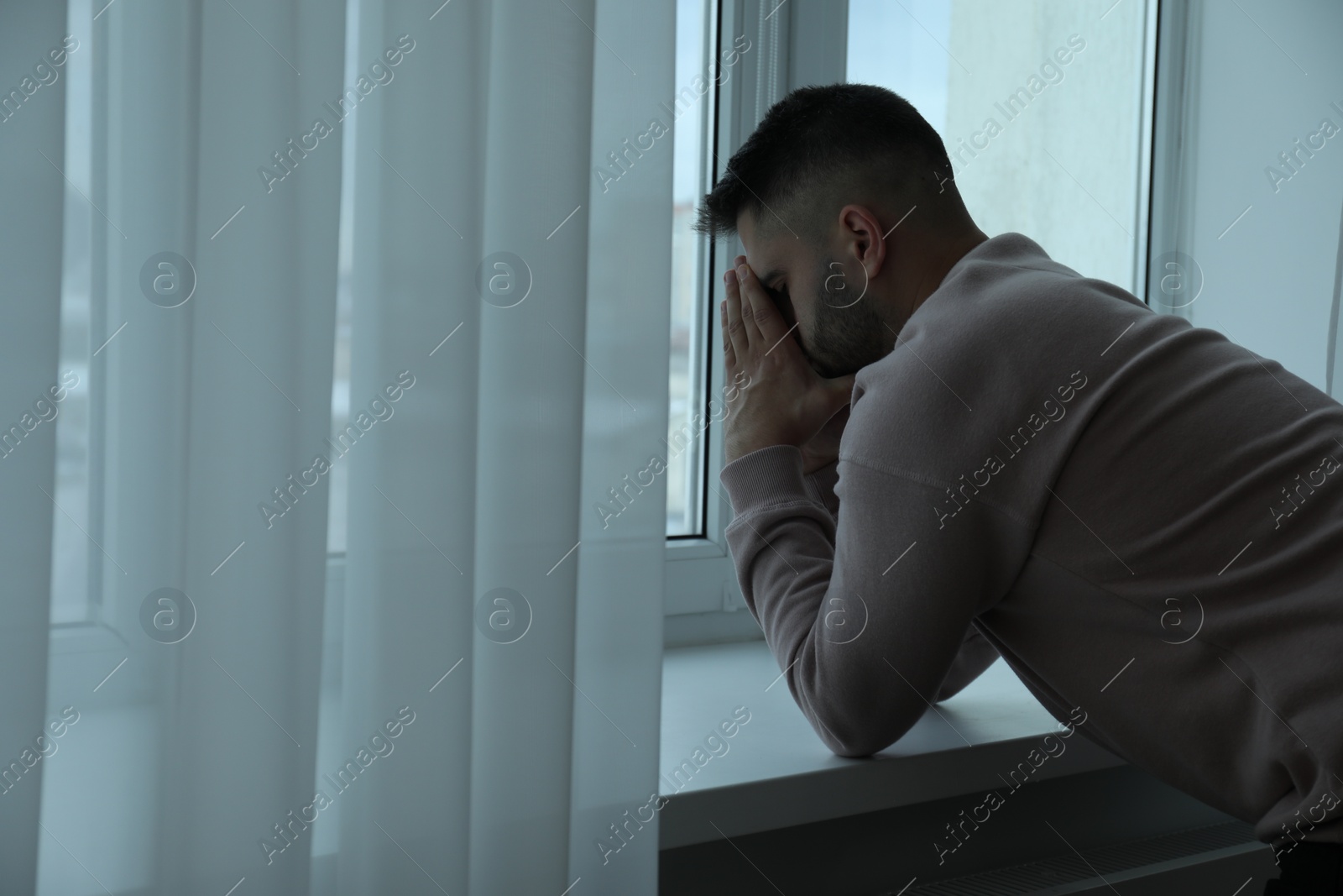 Photo of Sad man near window at home. Space for text