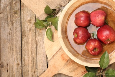 Photo of Fresh red apples in bowl with water and leaves on wooden table, flat lay. Space for text